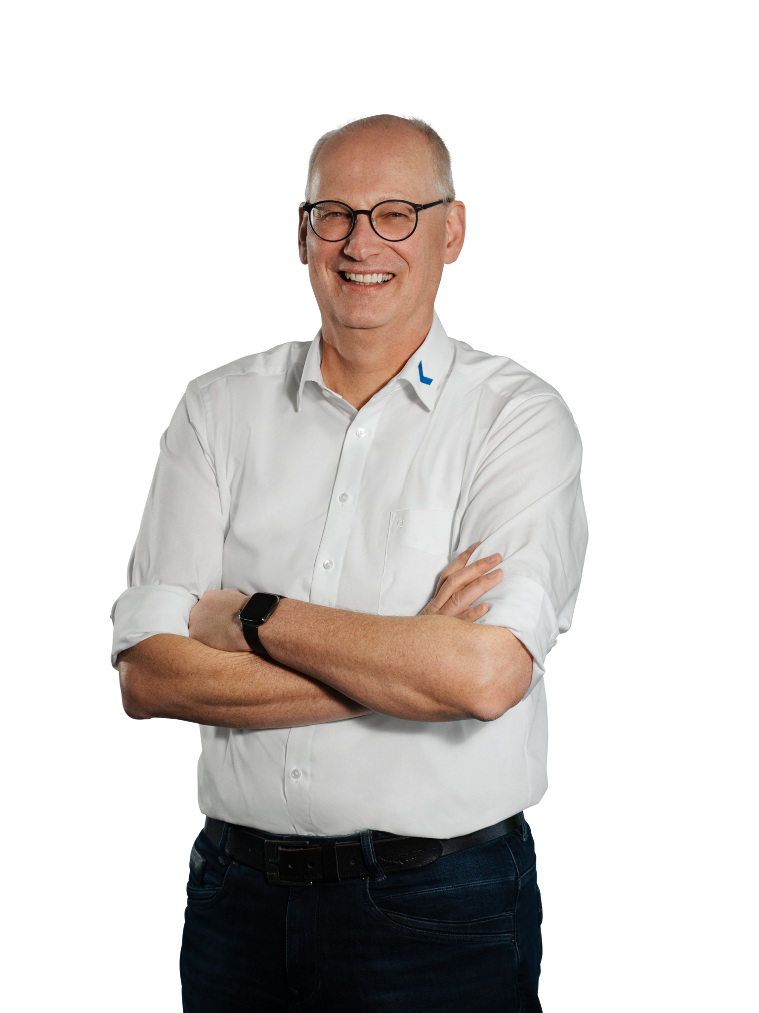 Een man in een wit overhemd, met zijn armen over elkaar en een bril op, glimlacht.