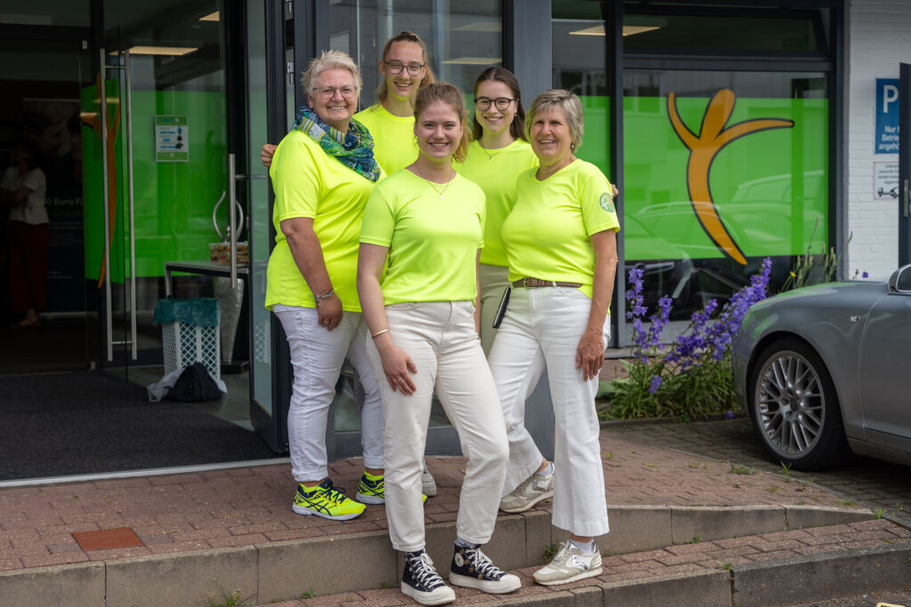 Vijf personen in gele T-shirts voor een gebouw.