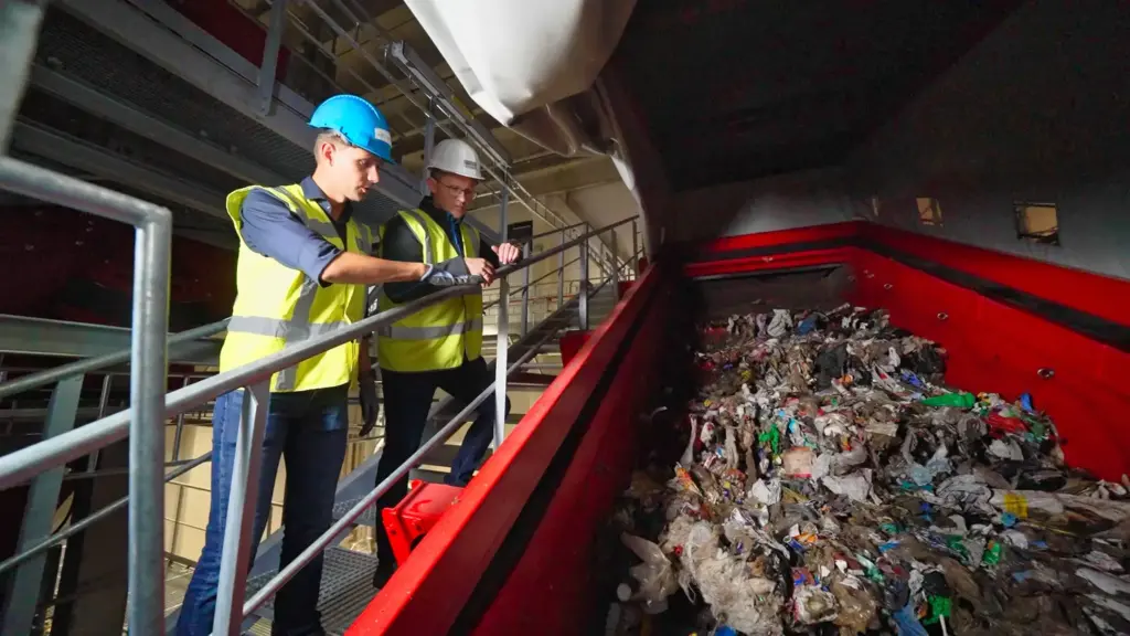 Twee recyclingdeskundigen bekijken een SPALECK-zeefmachine in een grote recyclinginstallatie voor huishoudelijk afval.