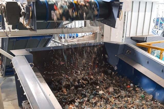 Het materiaal valt vanaf een transportband in een zeef met spanassen.