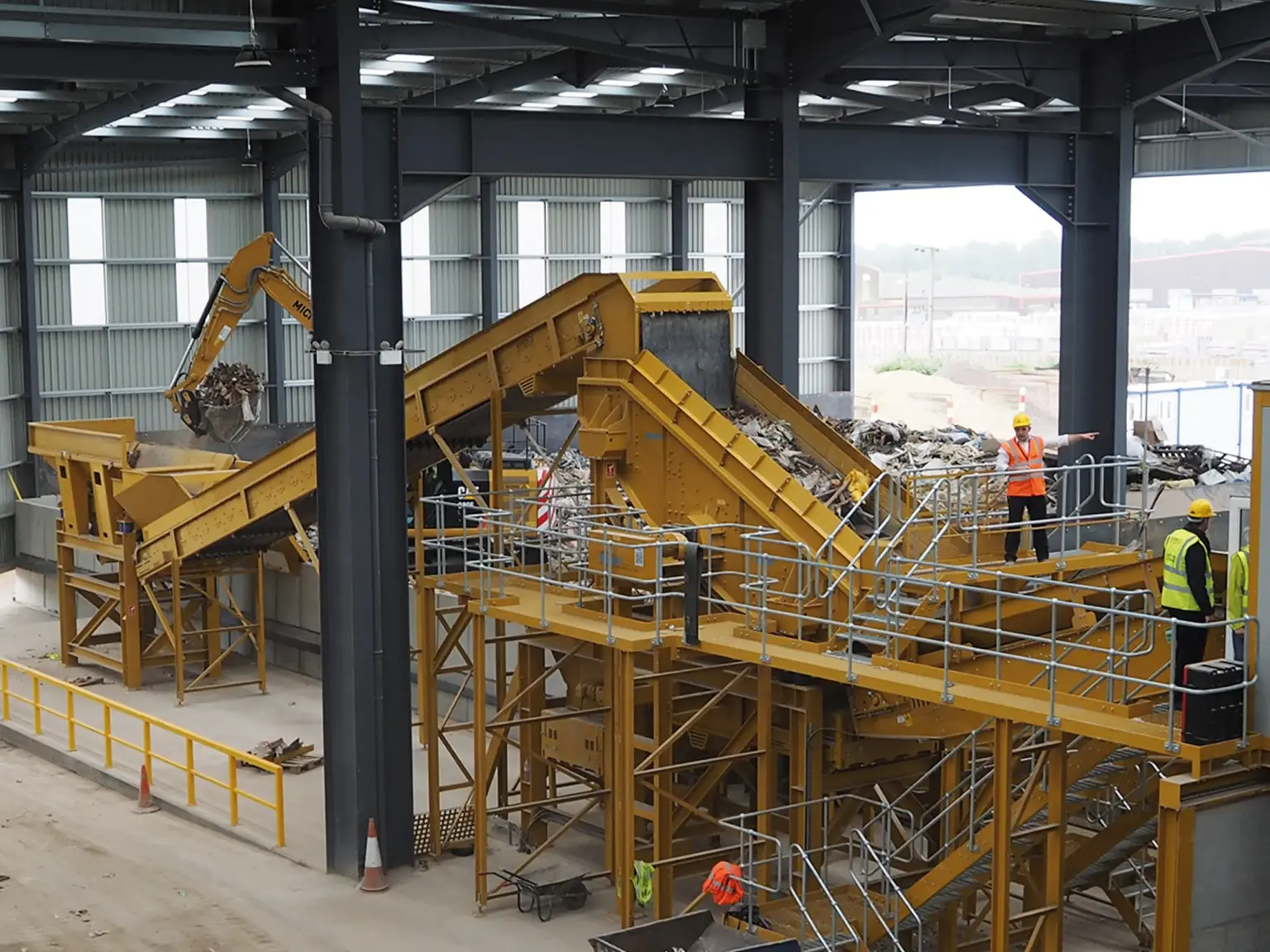 Industriële installatie met transportbanden en een zeef voor recyclebare materialen in een hal.