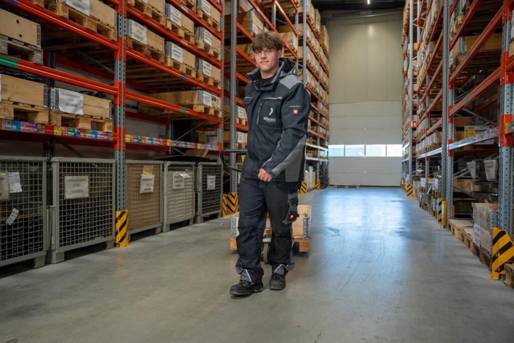 Een stagiair in de opleiding tot magazijnlogistiekmedewerker rijdt met een pallettruck door het magazijn
