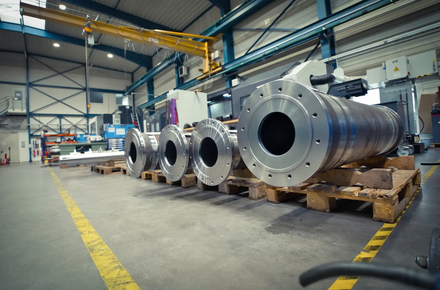 Grote metalen cilinders op pallets in een fabriekshal voor de bewerking van grote onderdelen met CNC-machines.