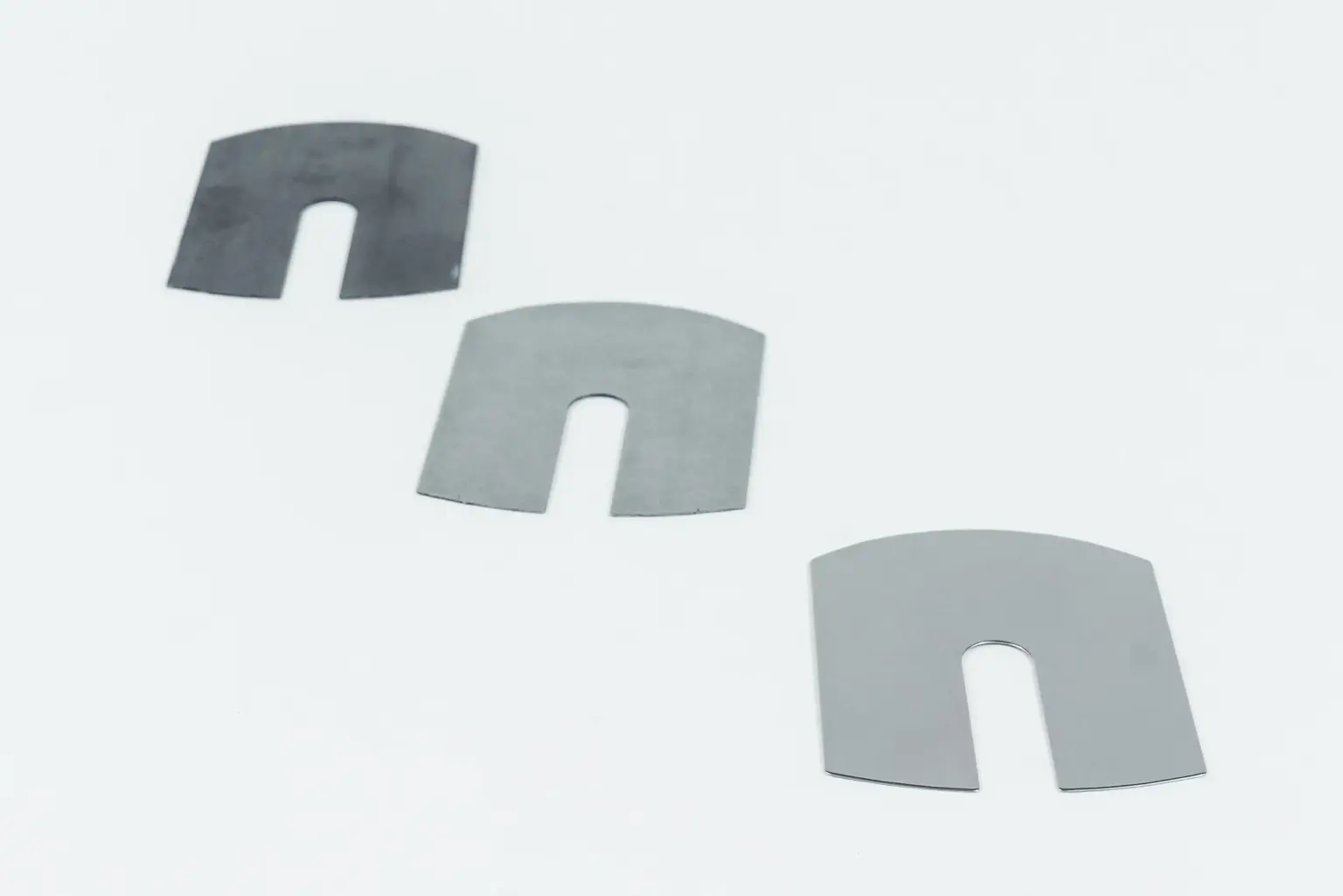 Drie metalen onderdelen met U-vormige uitsparingen op een witte achtergrond.