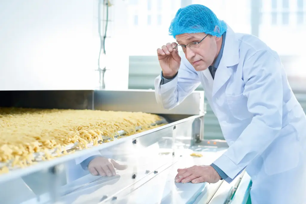 Een man in beschermende kleding inspecteert de voedselproductie.
