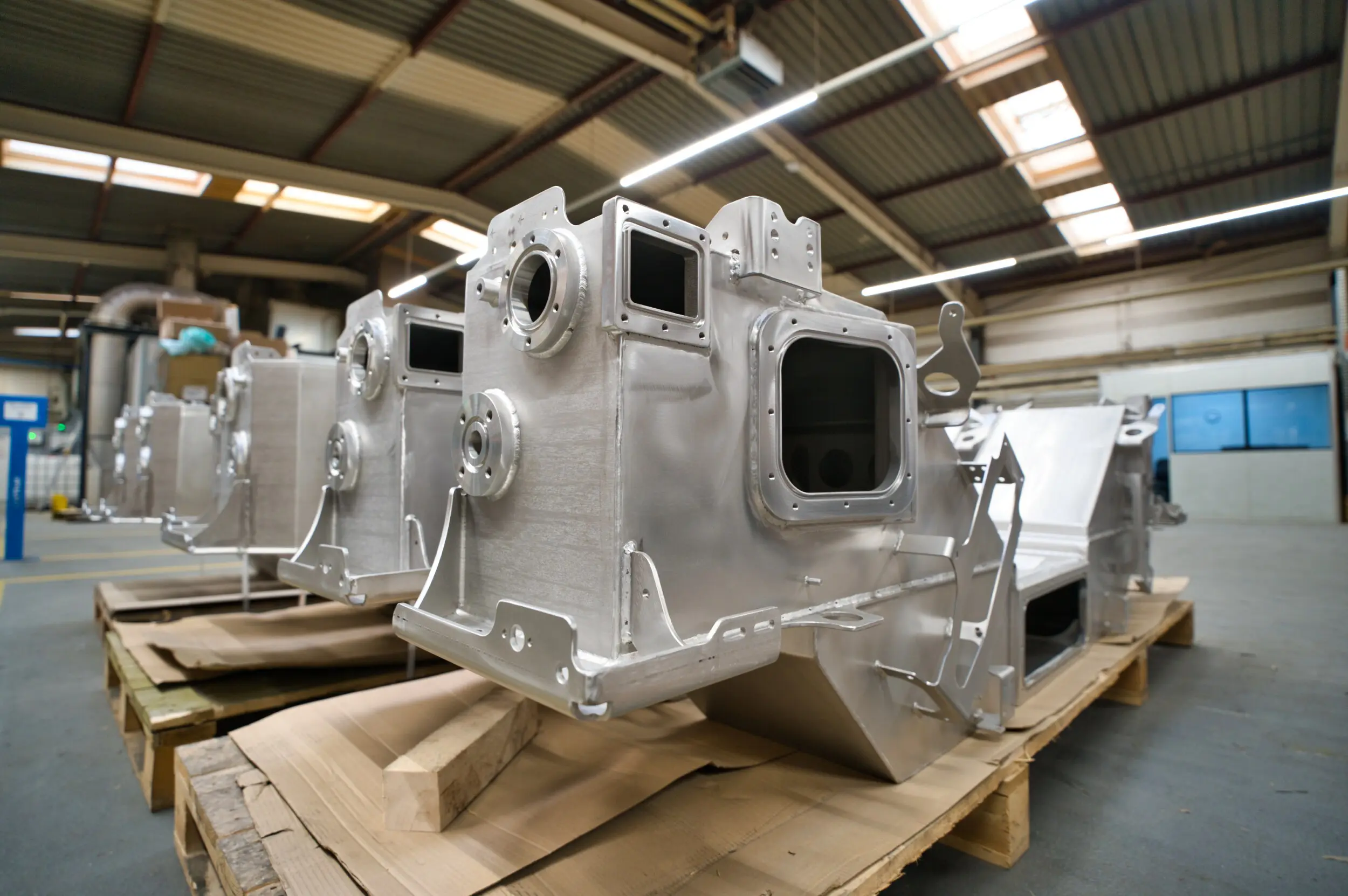 Grote metalen assemblages op pallets in een fabriekshal.