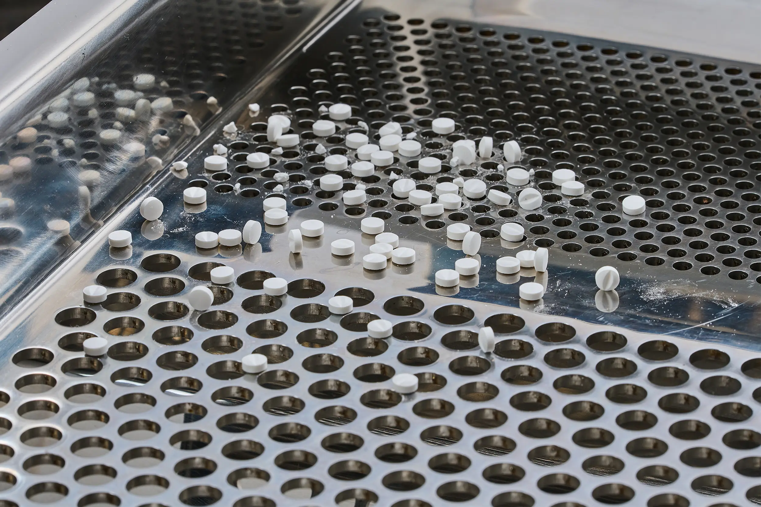 Witte tabletten op een metalen zeef in een farmaceutische zeefmachine.
