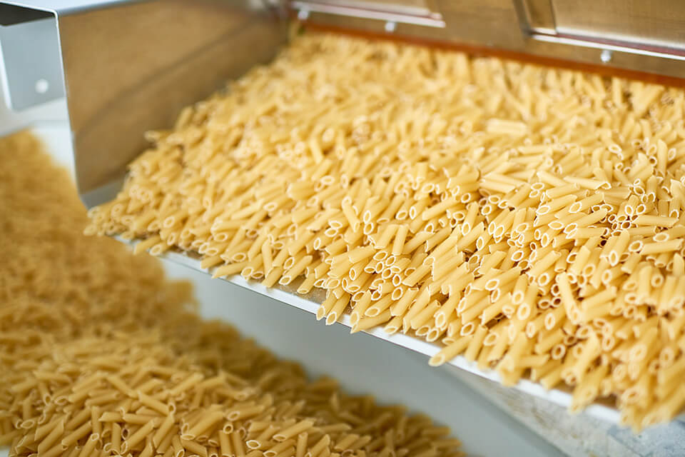 Pasta op een trilgoot in een productielijn.
