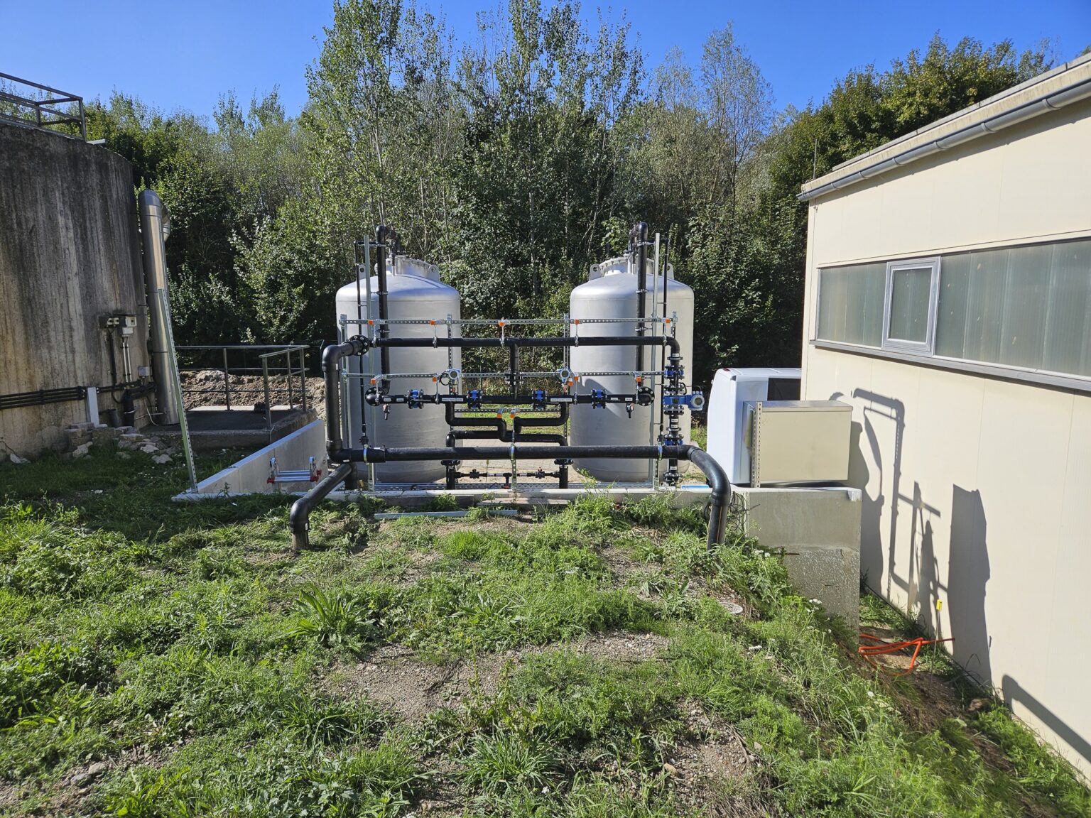 Twee tanks voor actieve-koolfiltratie met bijbehorende leidingen naast een fabriekshal.