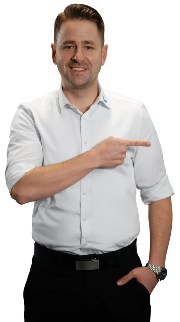 Een man in een wit overhemd wijst naar rechts; de aandacht is gericht op de metaalbewerking.
