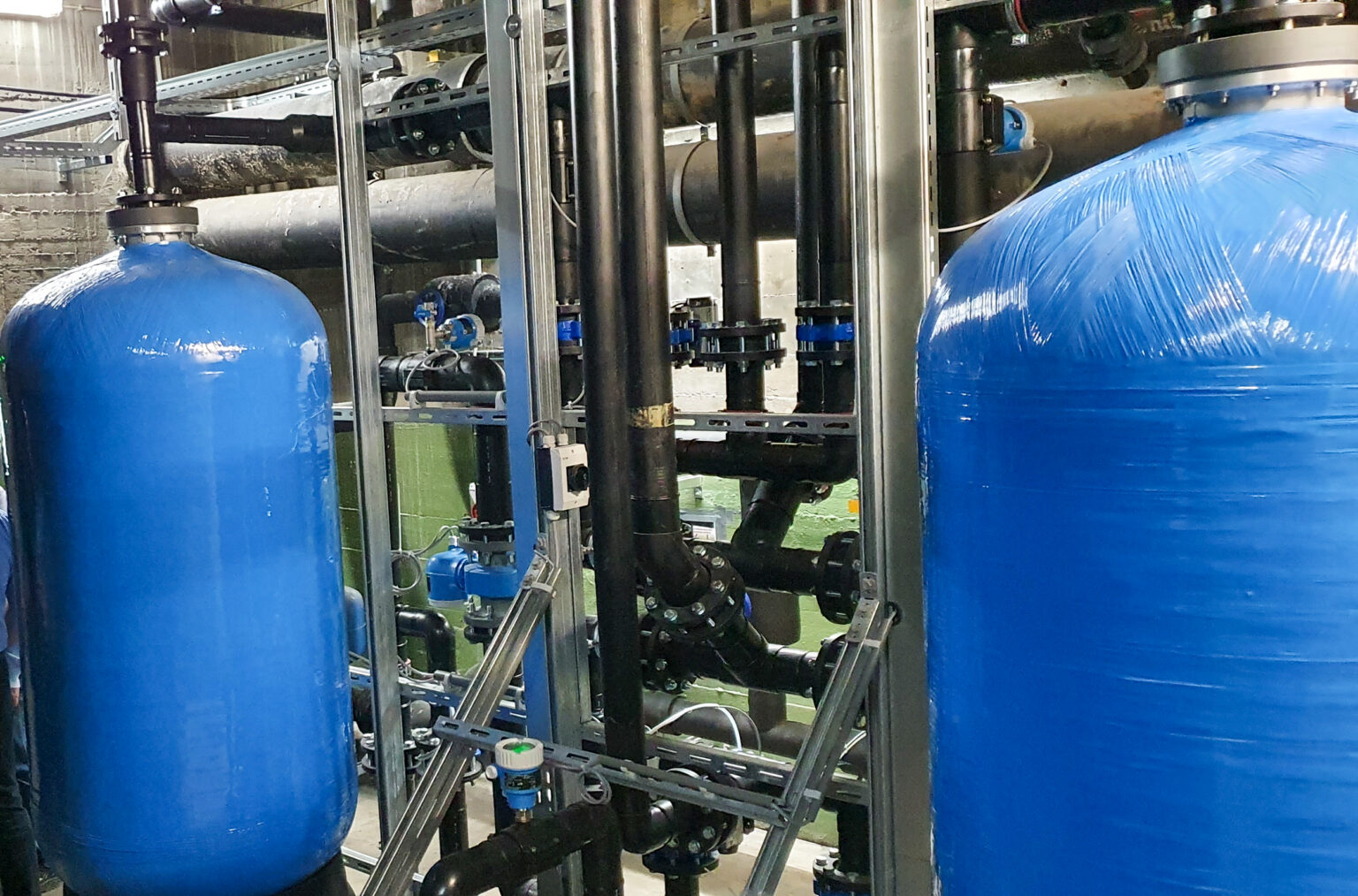 Zandfilterinstallatie met twee blauwe tanks en leidingen voor industriële waterzuivering.