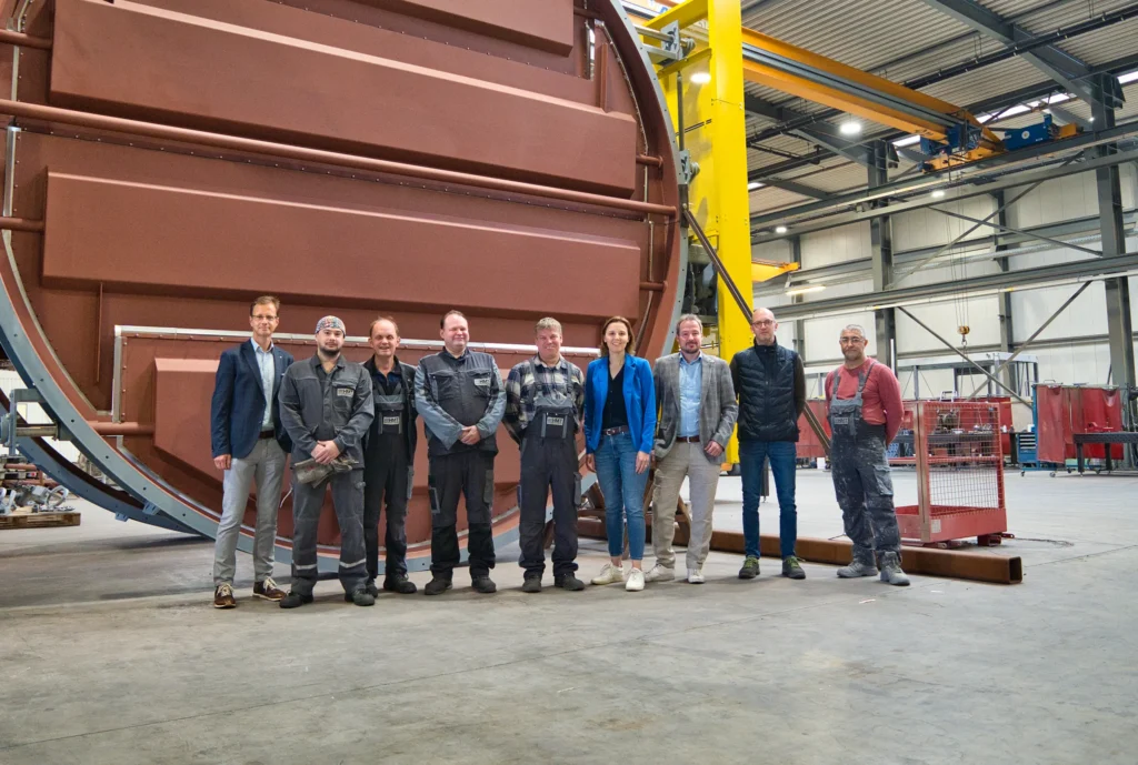 Een groep mensen staat voor een grote industriële machine in een fabriekshal.