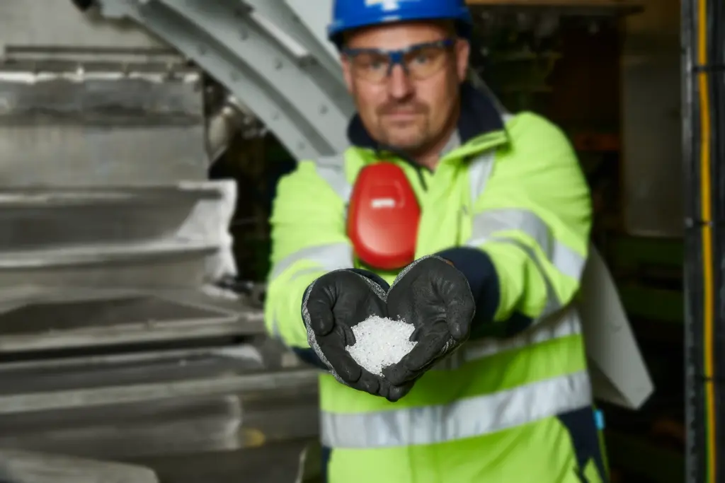 Een productiemedewerker van een fabrikant van kunststofgranulaat houdt vers geproduceerd en gecontroleerd gezeefd granulaat voor de camera
