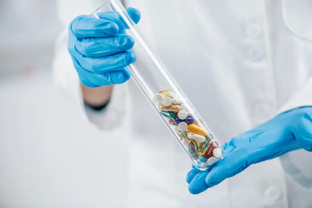 Een medewerker houdt een reageerbuis met diverse pillen vast – symbolische afbeelding van de farmaceutische industrie