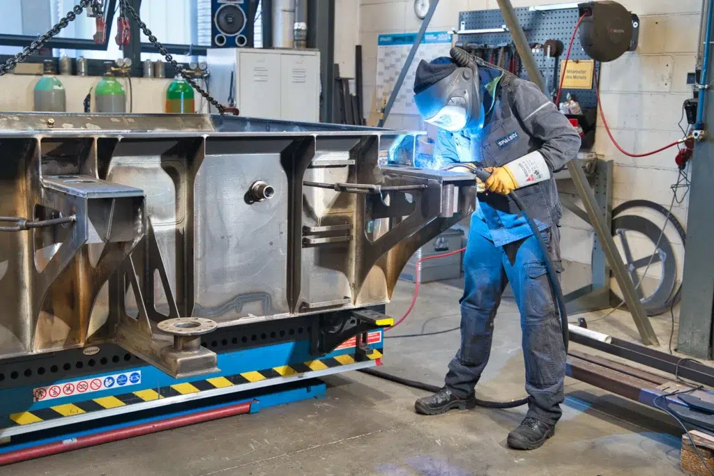 Een arbeider las een groot metalen onderdeel in de werkplaats.