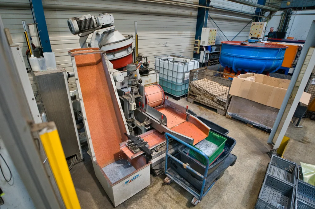 Industriehal met een glijslipmachine en een blauwe trommel op de achtergrond.